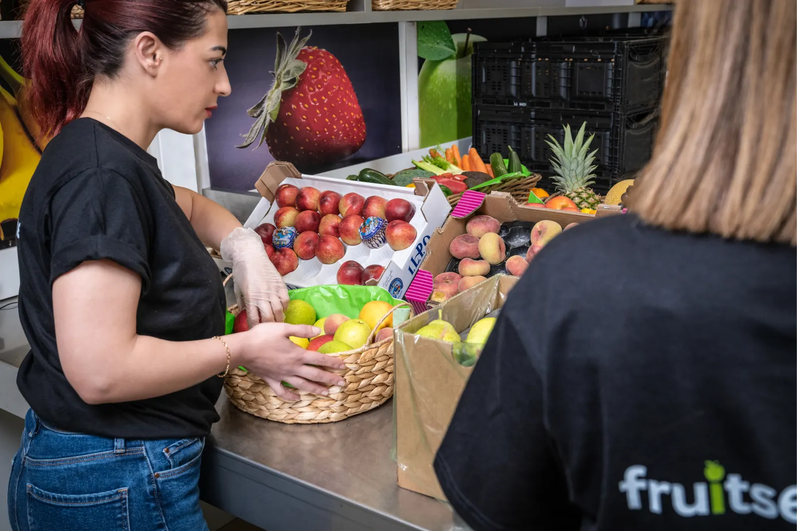 Mitarbeiterinnen bereiten Firmenfrüchte-Körbe mit frischen Früchten vor